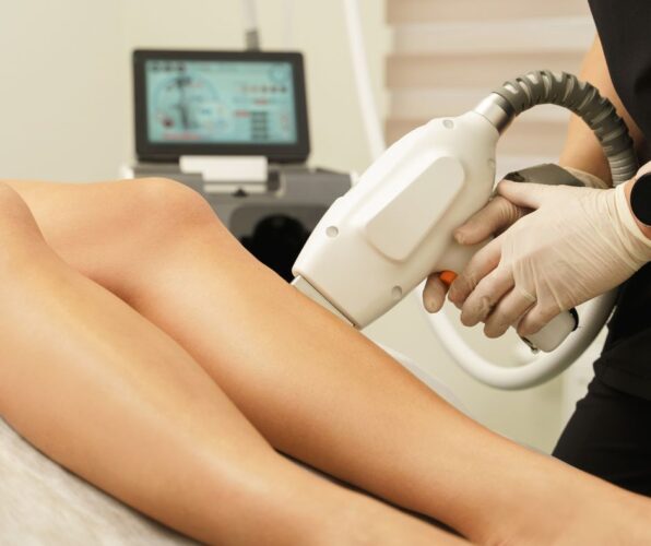 Aesthetic therapist applying precision laser handpiece to client leg during accredited laser hair removal training.